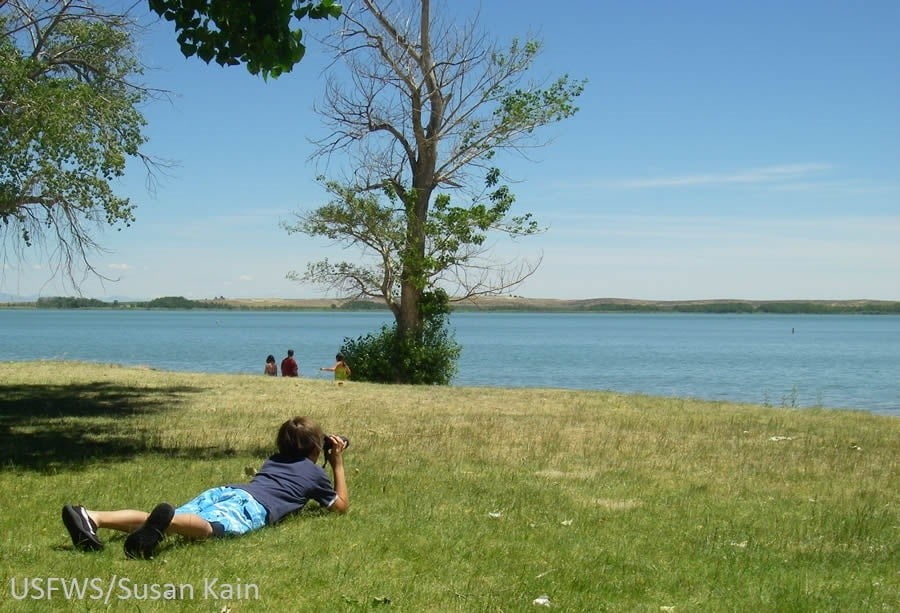 boy looking out binoculars over a lake