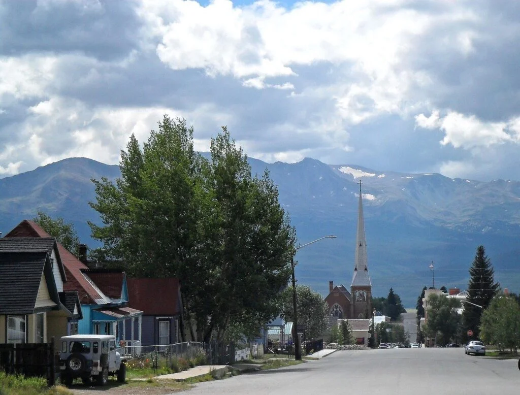 looking down a small town street with tall white steeple straight ahead, talk mountains behind