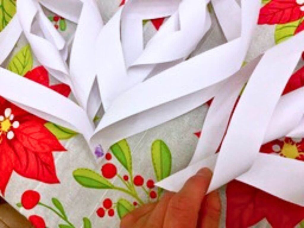 connecting individual pieces of shaped white paper to create a giant paper snowflake atop a poinsettia designed tablecloth. The picture is kind of fuzzy