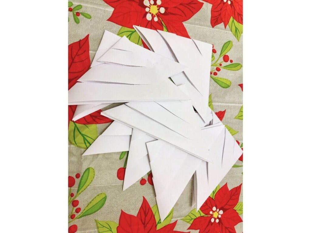 papers folded into triangles with straight cuts every half inch through them, atop a poinsettia design tablecloth
