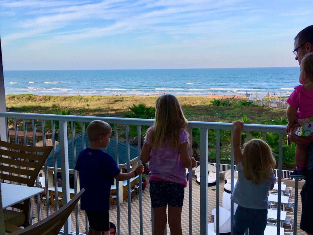 Affordable family vacation in South Padre; family looking over balcony at the ocean