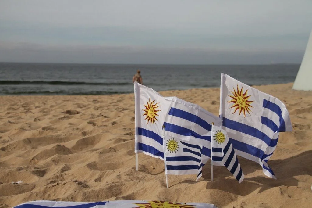 Uruguay flags (white/blue stripes with yellow sun) in the sand