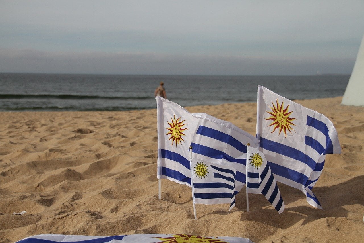 Uruguay flags (white/blue stripes with yellow sun) in the sand