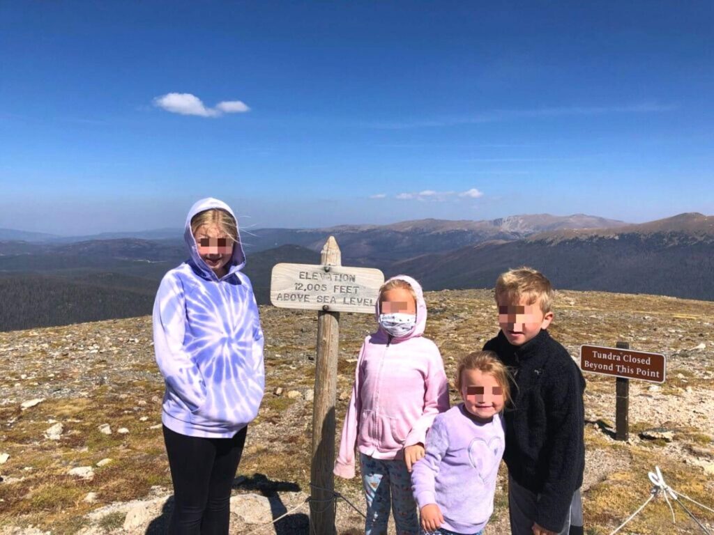 kids standing in front of an "elevation 12,005 feet above sea level" sign, mountain tops in the distance