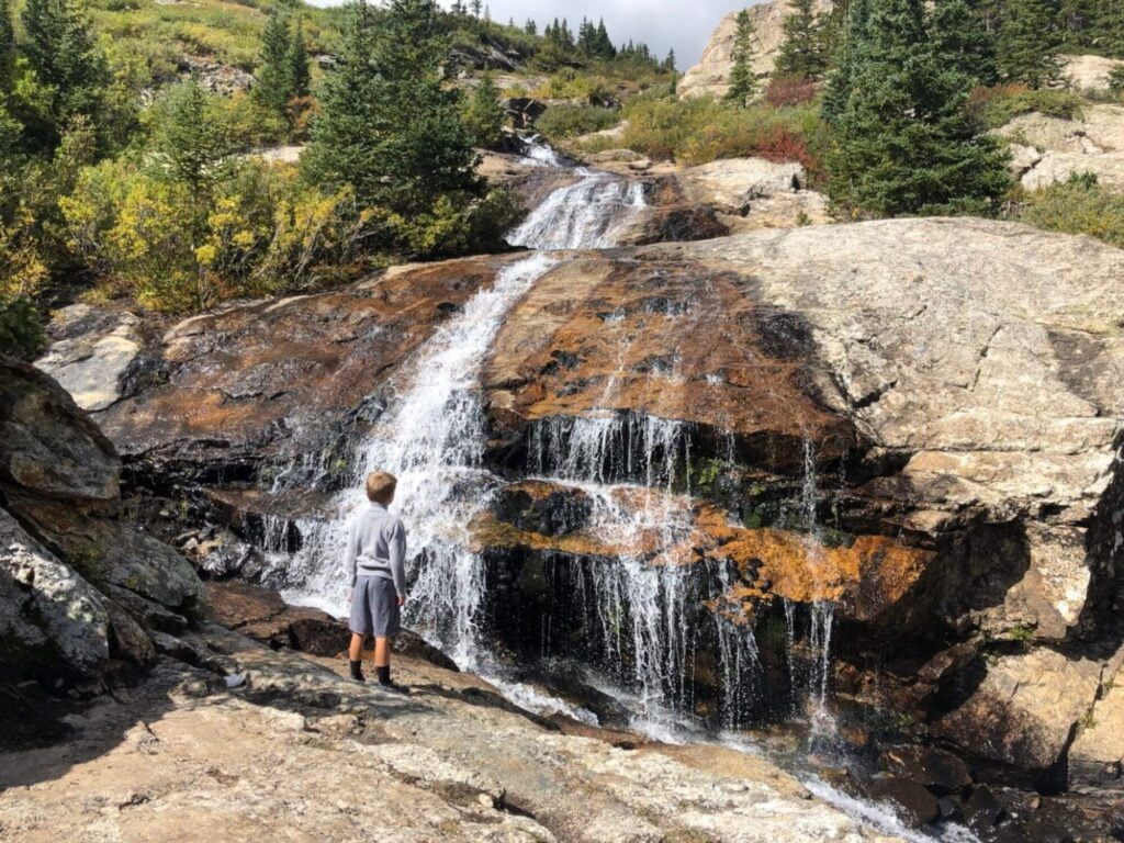 boy standing at waterfall coming down rocks at Blue Lakes Breckenridge CO