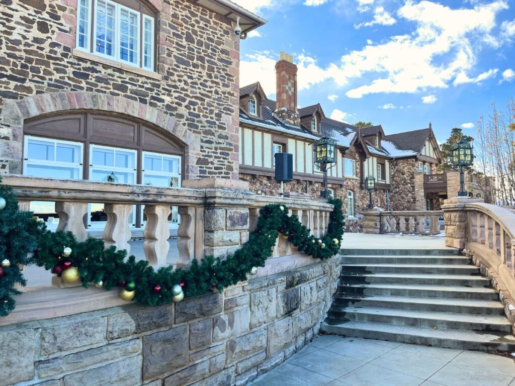 The Highlands Ranch Mansion at Christmas. A long garland is draped on the stone fence towards steps that go up to the entrance of the mansion