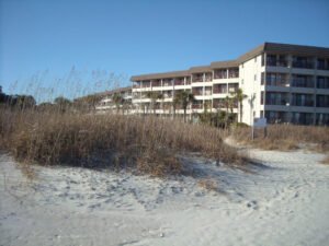 beachfront rental in hilton head, white sand on bottom, dry brown grasses in middle, white condo complex and blue sky