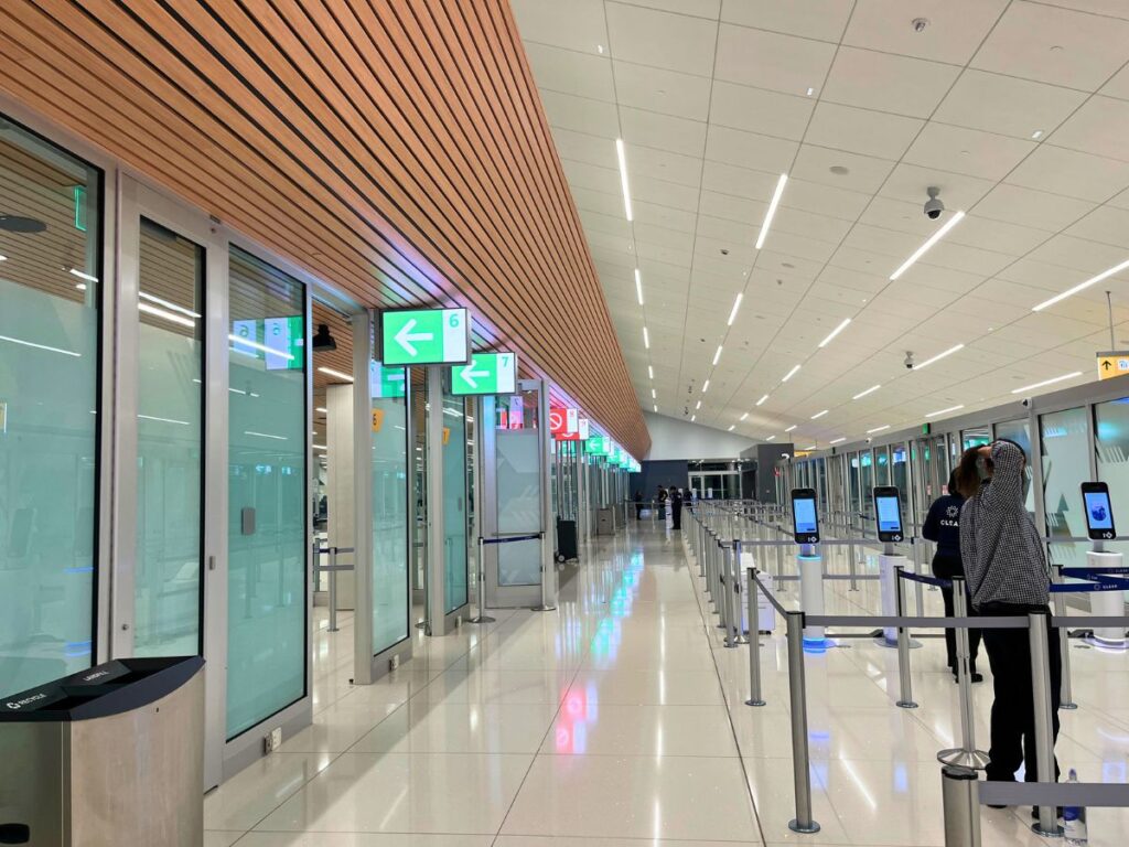 looking into an empty area at airport security at the Denver airport.  White floors, white ceilings, and arrows in green above different openings to guide travelers.