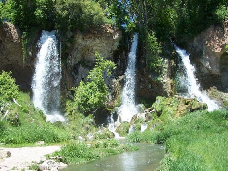 3 tall waterfalls dropping a few meters apart with lush green grasses and bushes