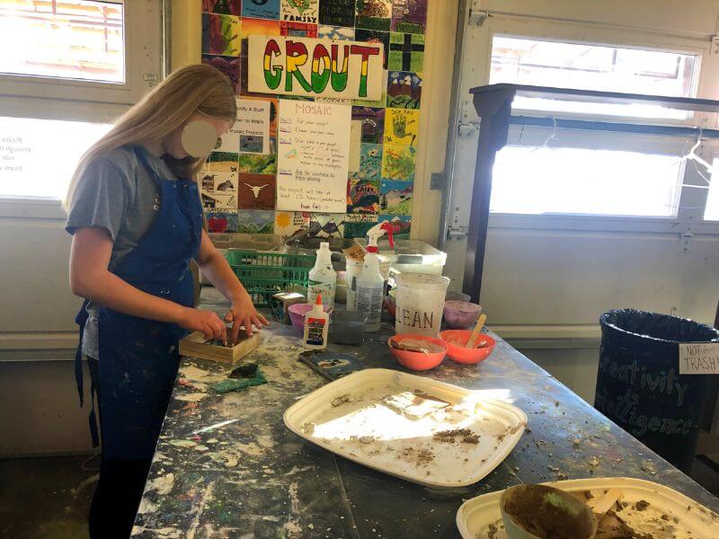 girl standing at messy art table working grout into a small wodden box