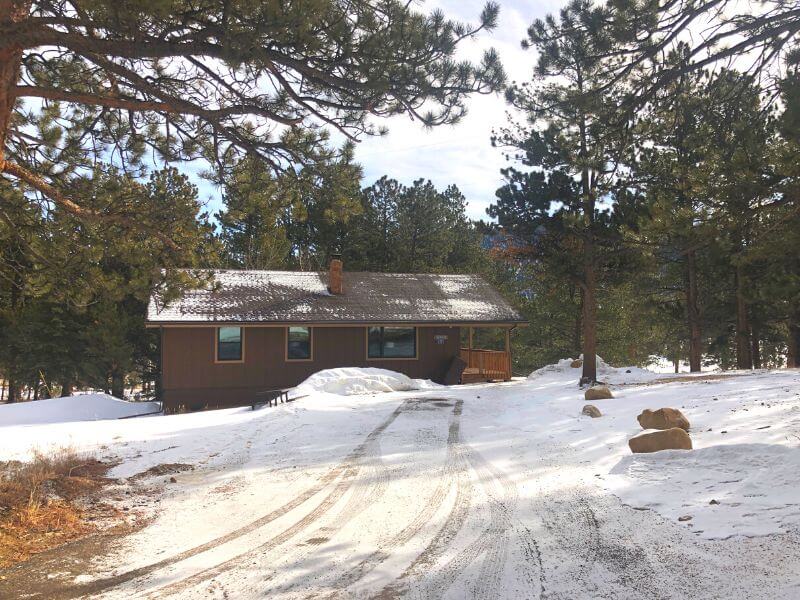 exterior of wooden cabin in the snow with tall pine trees surrounding at YMCA of the Rockies Estes Park