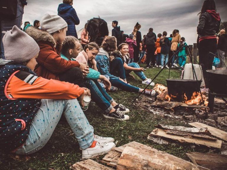 lots of kids sitting on ground in front of a fire at camp