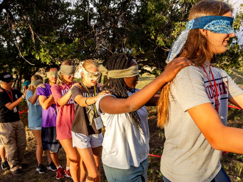 youth holding each others shoulders in a line with blind folds on