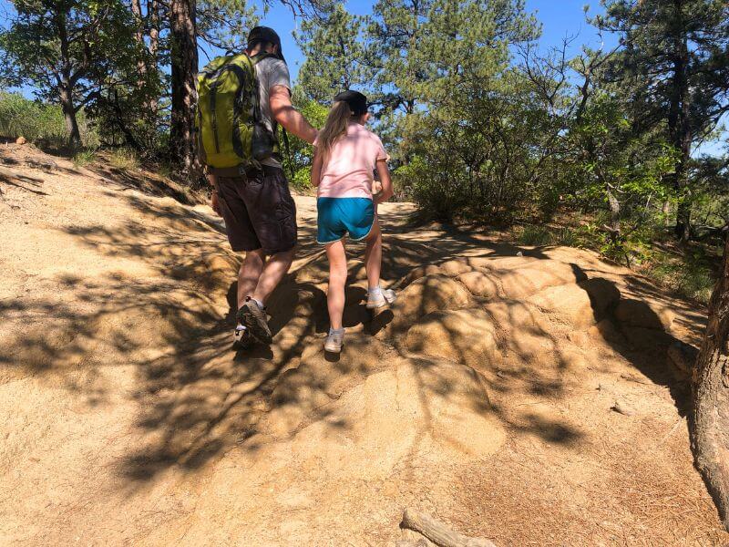 father and daughter hiking through shaded area on brown dirt path