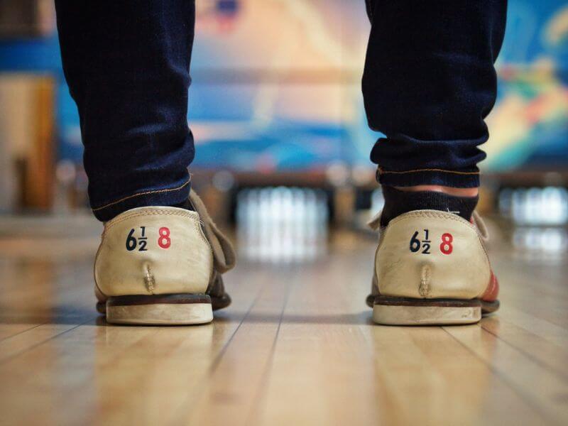 close up of the back of someone's bowling shoes as they stand at the end of a lane, about to bowl