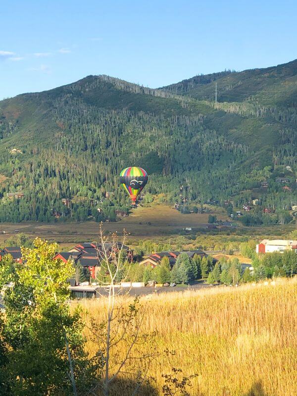 colorful hot air balloon floating above brown grass, with green mountain behind