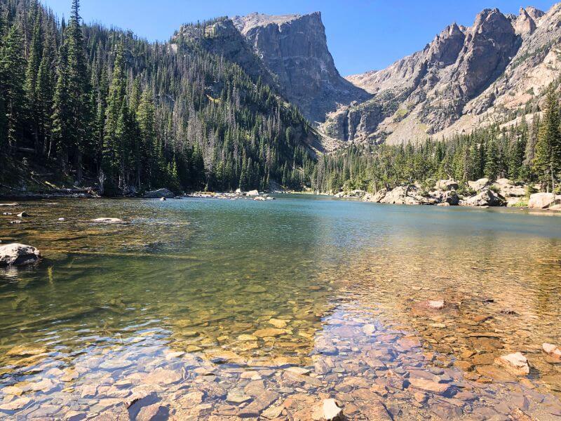 turquoise lake with rocks in foreground below water and tall sharp mountain peak in background