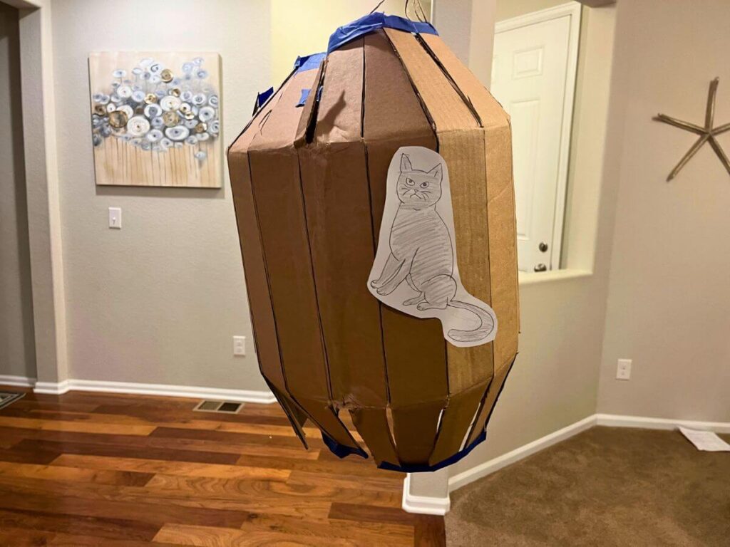 Denmark Fastelavn Cat in a Barrel- a cardboard barrel with a picture of a cat, hanging from the ceiling