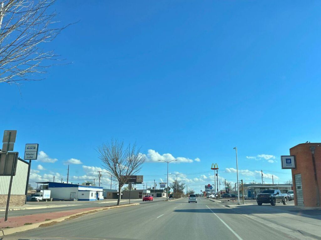 driving point of view with flat, straight road ahead, a McDonalds sign high in the sky in the distance, a  few cars on the road and a small buildings along the side