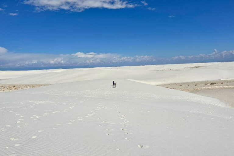 two kids in the far distance running across white sand, blue skies with one cloud at top at White Sands National Park