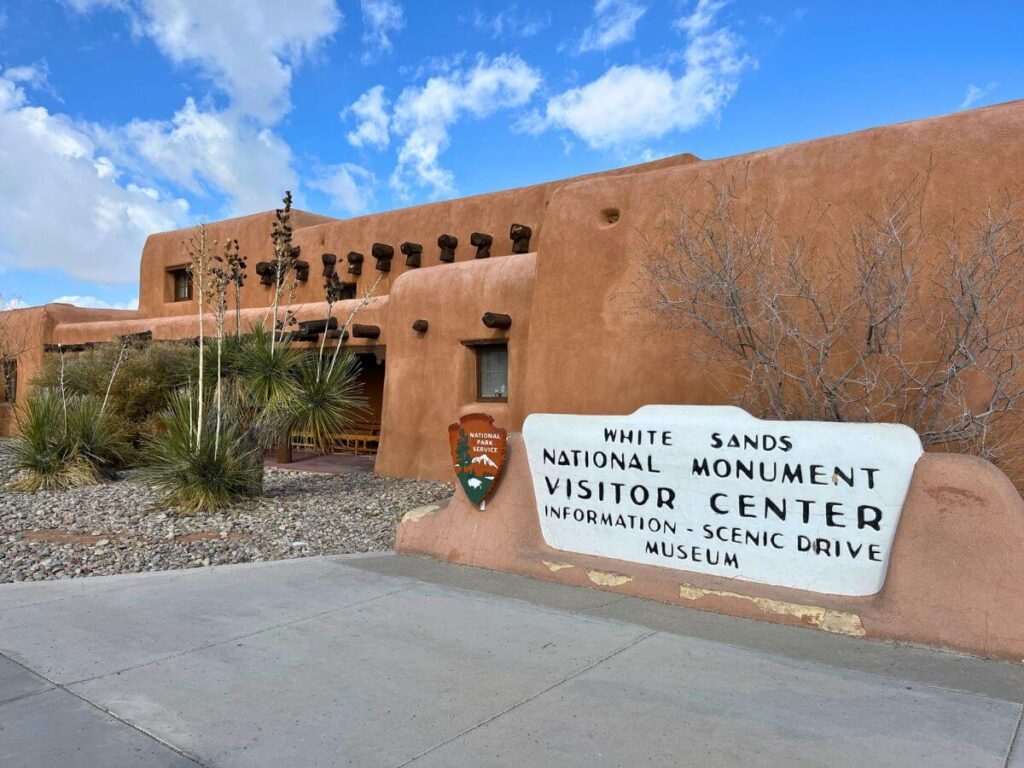 red/orange adobe style building with White Sands National Park sign in the foreground