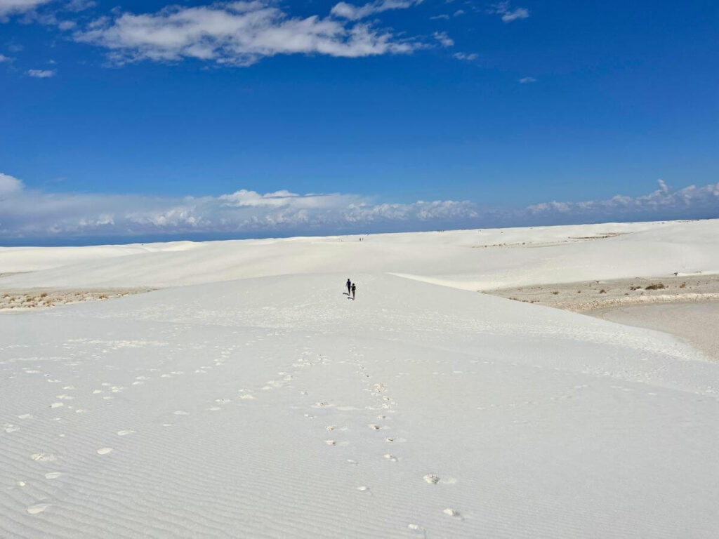 two kids in the far distance running across white sand, blue skies with one cloud at top