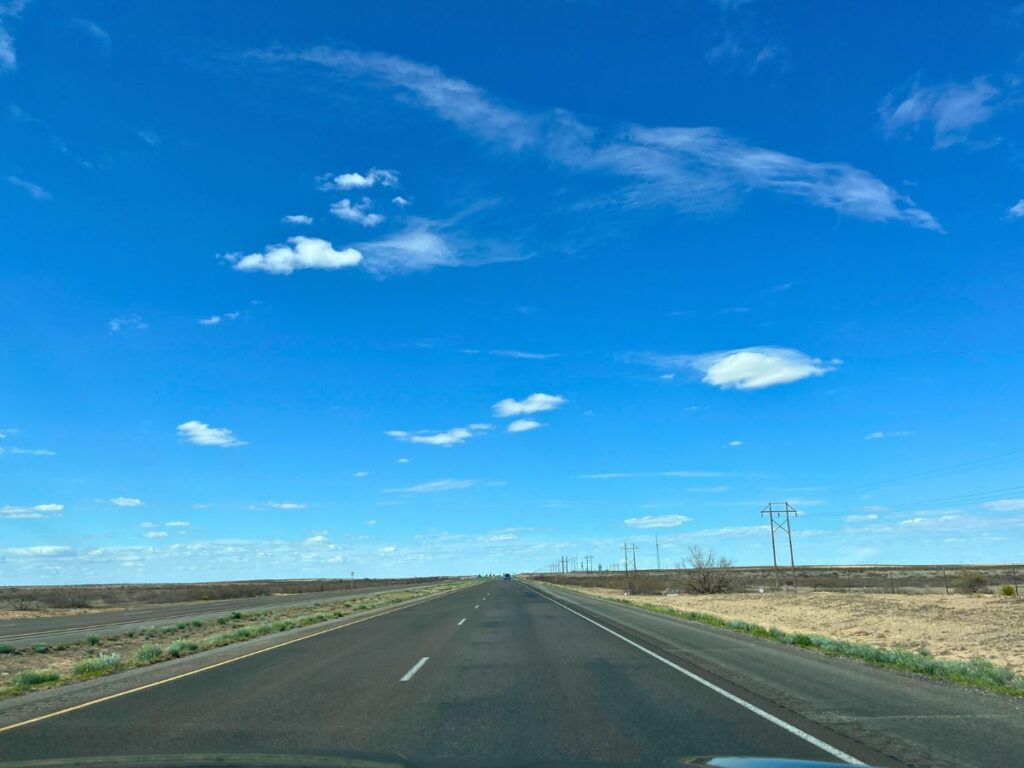empty 2 lane road with blue skies and just a couple small random clouds, barren on the sides of the road