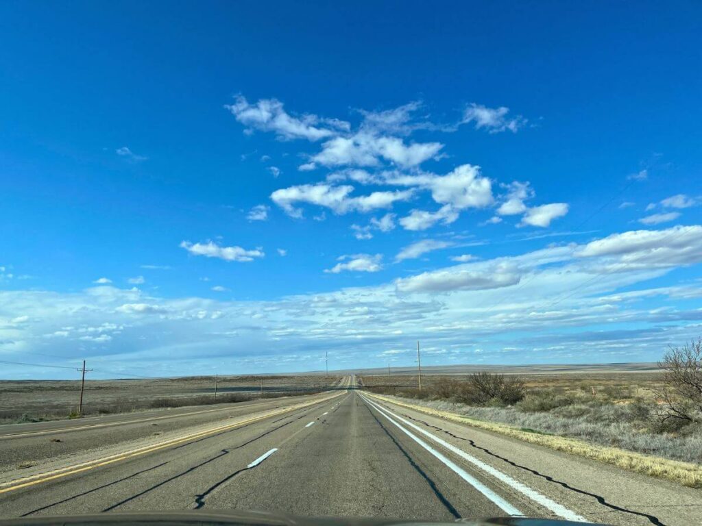 4 lane highway with no cars, blue skies with a couple small clouds, brown grasses on the side of the road