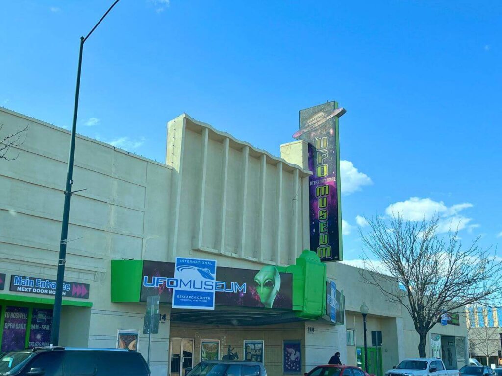 large tan building with flat front and banner signs hanging above entrance with alien faces noting the UFO center