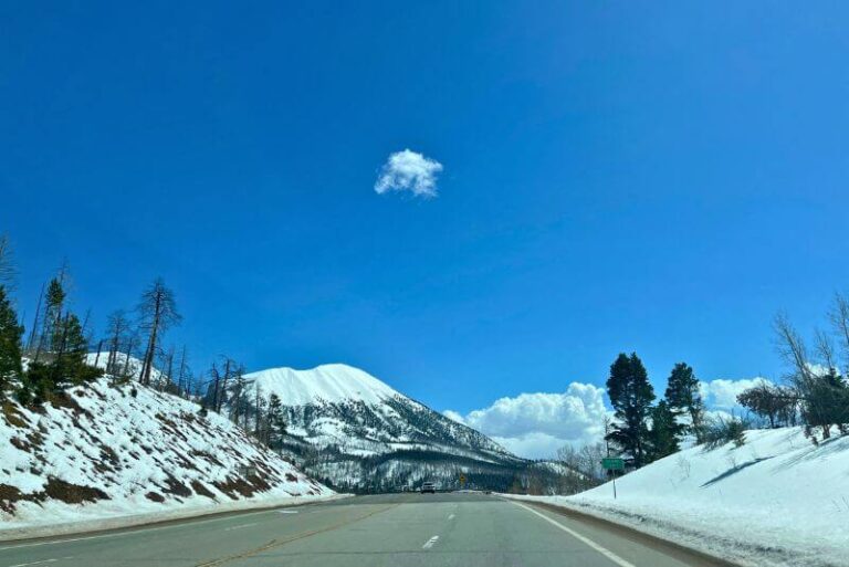 stretch of road with snow on side hills of road and ahead on a mountain