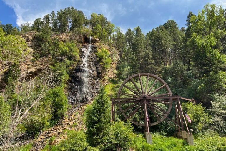Large water wheel in center with a light waterfall to the left coming off the top of the mountain