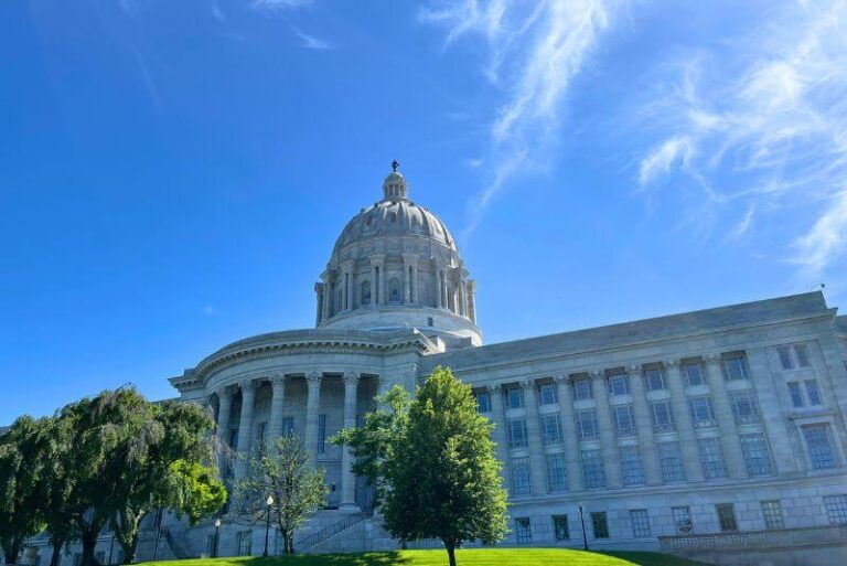 large capitol building in Jefferson City, MO. A few green trees in front, angled up slightly looking to the blue sky