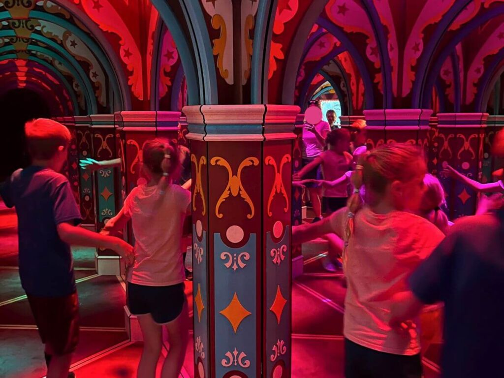 Entire picture has a red light hue to it. Kids walking around inside a mirror maze, so you can see a few sets of the same kids within the image