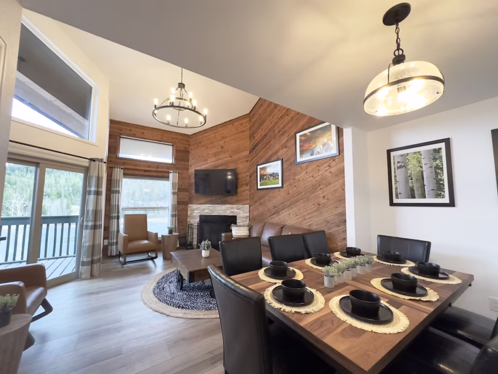 looking at a large condo unit at Beaver Meadows resort in Colorado. Nearby is a square table with 8 black seats around it, wood flooring, a living area that rises 2 stories with a fireplace in the corner