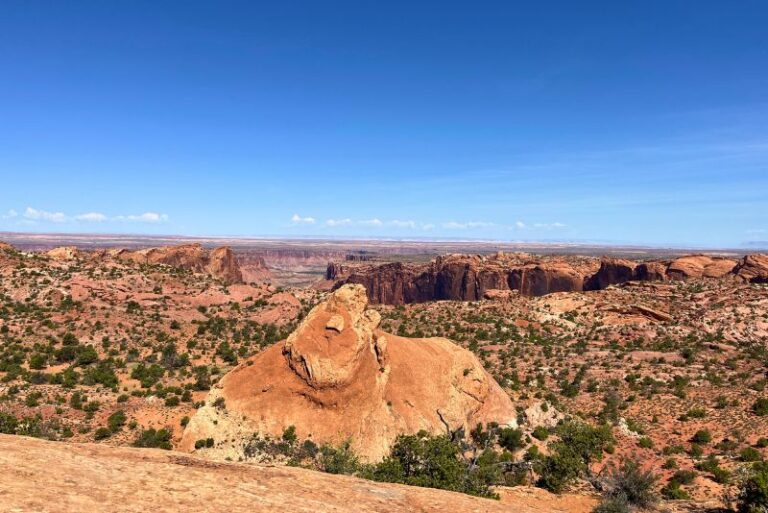 view at Canyonlands. Large rock formation in middle, flat ground around and a few tall mountain walls beyond
