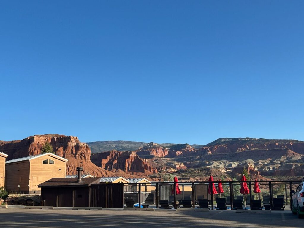distant view of a pool behind a metal fence with red patio umbrellas, red rock formations in the background