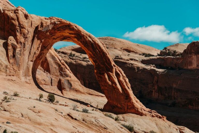 Corona Arch in Moab is a sandstone arch coming out of the rock on the left, a cliff drops to the right