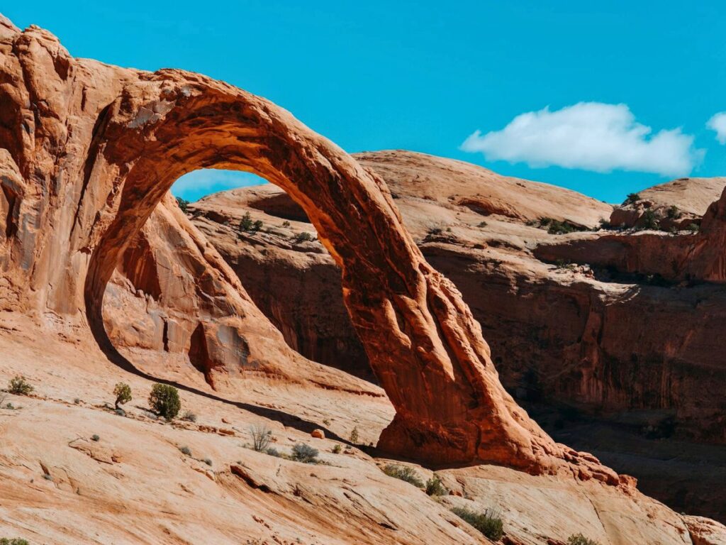 Corona Arch in Moab is a sandstone arch coming out of the rock on the left, a cliff drops to the right