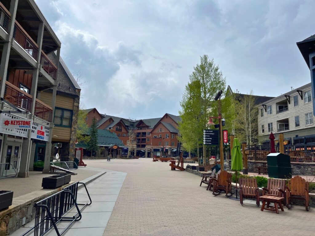looking down the pedestrian area of River Run Village in Keystone, CO in summer. Restaurants and shops to the side, with a few table and chairs outside