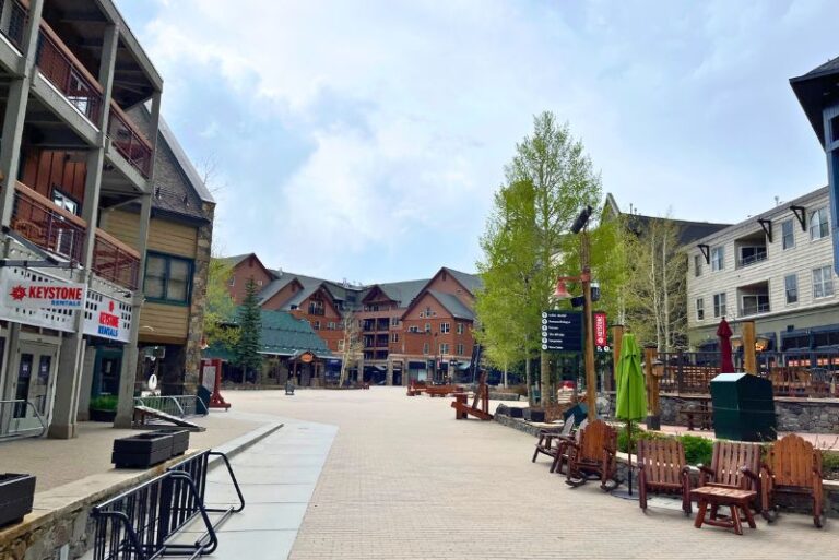 looking down the pedestrian area of River Run Village in Keystone, CO in summer. Restaurants and shops to the side, with a few table and chairs outside
