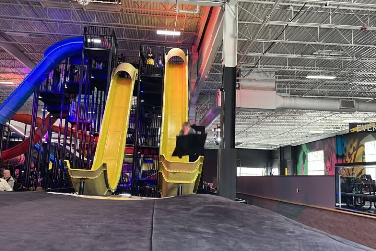 two steep yellow indoor slides. A child is launching off the end of one onto a black mat at Slick City Denver