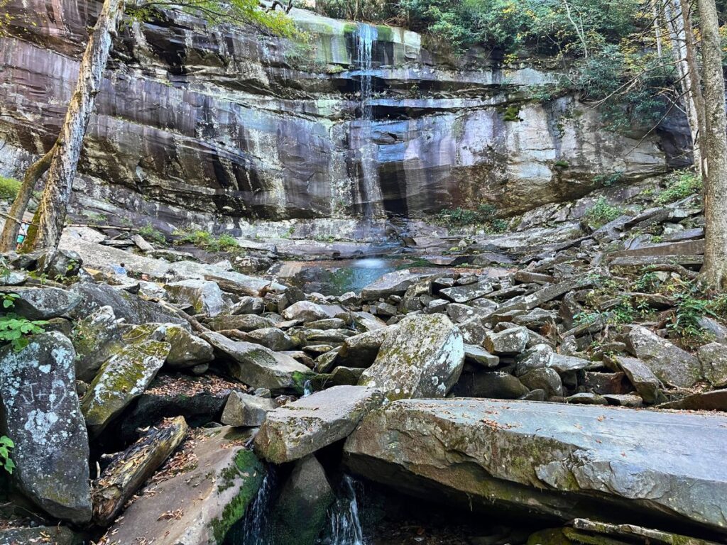 Rainbow Falls in Great Smoky Mountains National Park. A smooth cliff wall with burned sections and a light waterfall coming down. Many large rocks in front