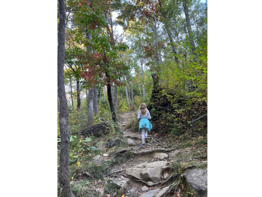 a little girl hiking through a rocky area with tall colorful trees at the Rainbow Falls Trail at Great Smoky Mountain National Park