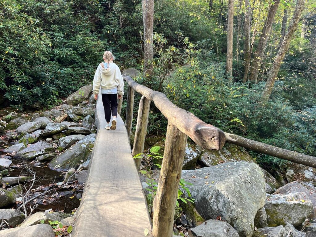 a girl crossing a flattened log made into a bridge across a little creek