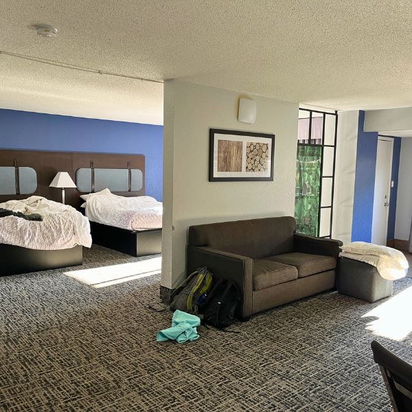 a large hotel room with a couch against a section of wall and two beds on the other side of the wall
