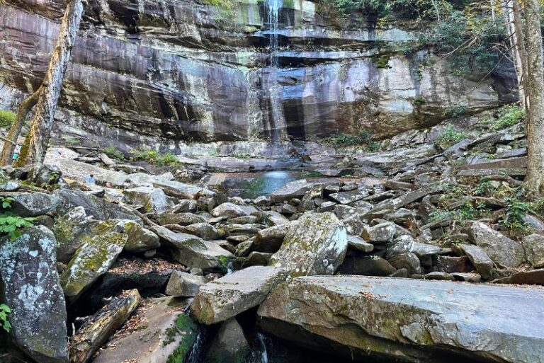 Rainbow Falls in Great Smoky Mountains National Park. A smooth cliff wall with burned sections and a light waterfall coming down. Many large rocks in front