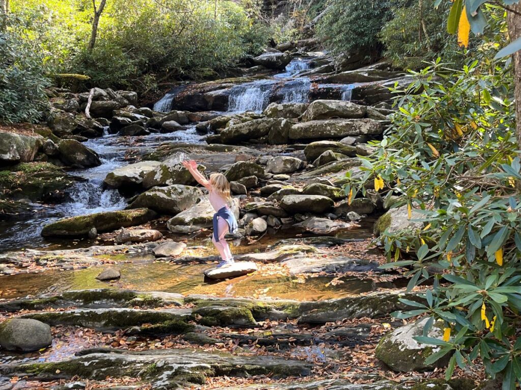 a young girl throwing a handful of water up in the air as she stands in front of the Chimney Tops waterfall in Great Smoky Mountains National Park