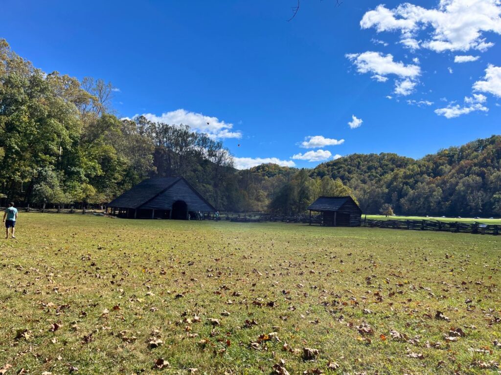 Mountain Farm Museum is a great stop if you have 1 day in Great Smoky Mountains National Park. A flat, grassy area with two historic cabin-like structures in the distance