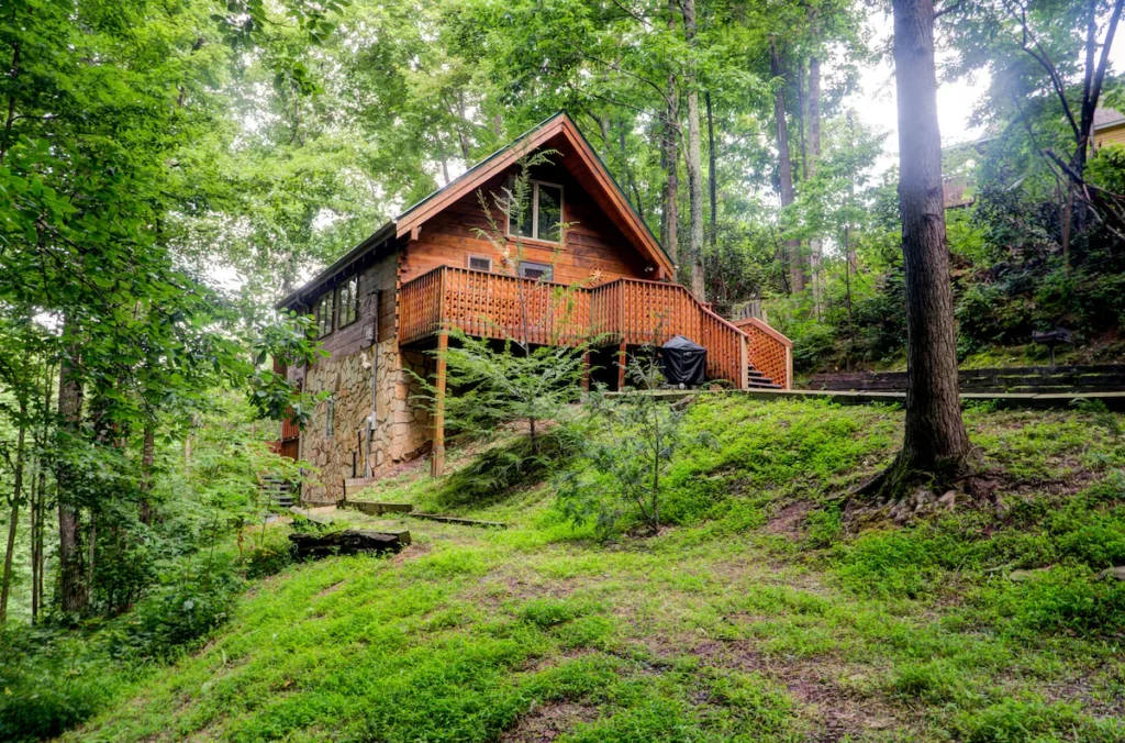 an a-frame cabin sits among trees and green groundcover in Gatlinburg