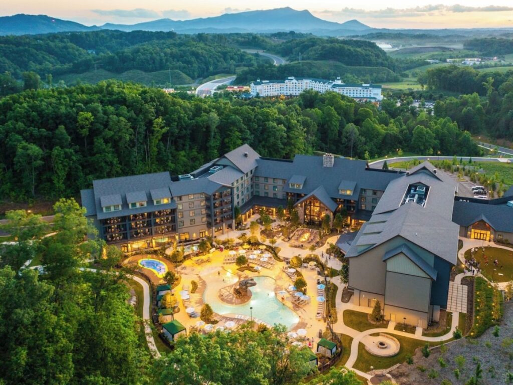a drone photo of Heartsong Lodge in Pigeon Forge, TN at dusk.  The pool area is in the center with the lodge wrapping around 3/4 of the pool area.  The lodge is surrounded by trees.  Heartsong is one of the best places to stay in Great Smoky Mountains